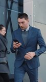 Caucasian Businessman in a Suit is Using a Smartphone on Dark Street in the Evening. Other Office People Walk Past. Video Footage with Vertical Screen Orientation 9:16.
