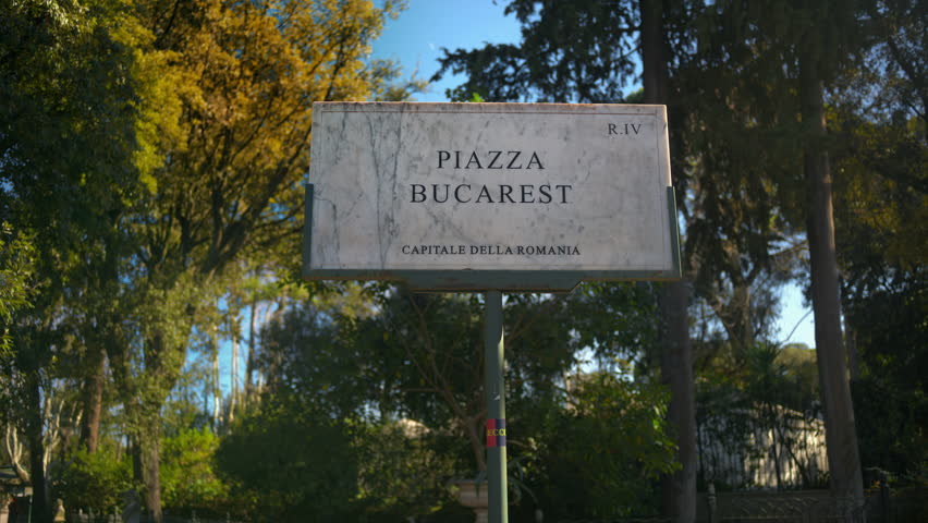 Marble sign of Bucharest square. Translation "Bucharest square, the capital of Romania" surrounded by trees in sunlight. Rome, Italy