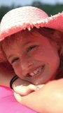 A little happy girl wearing a pink straw hat lying on an inflatable pink sofa on a Sunny beach.