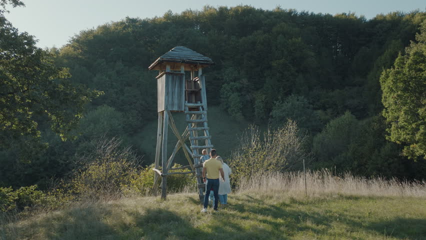 Young family climbing up the wodden observation tower by the forest in the countryside. Fun family acitivity on a sunny summer day. 