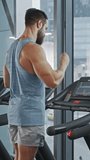 Muscular Male Athlete Inserts Wireless Headphones, Turns on Podcast or Music Playlist with Smartphone and Starts Running on a Treadmill. Leg and Cardio Gym Day. ertical Screen Orientation Video 9:16
