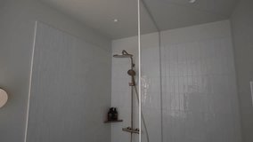 Cesis, Latvia - February 14, 2024 - A modern bathroom shower with gold fixtures, white tiles, and a glass door. On the side, a radiator and shampoo bottles are visible.