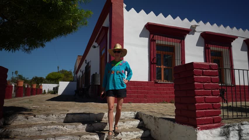 Female tourist wearing straw hat and ethnic, traditional clothes walking in front of historical building in mining town of El Triunfo, Mexico.