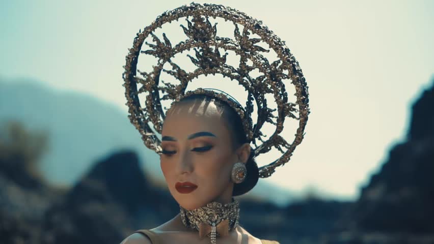 Woman with avant-garde headpiece and makeup posing in a dramatic outdoor setting during the daylight