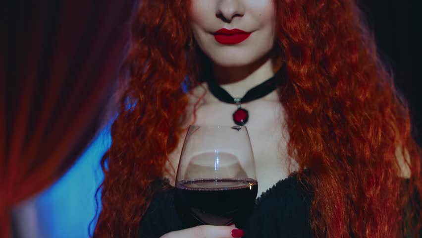 gothic woman red-haired mystical beauty red lips close-up, hand holding glass of red wine. Dark night room. Fantasy lady vampire girl evil smiling sexy face evening makeup red nails black dress art 4k