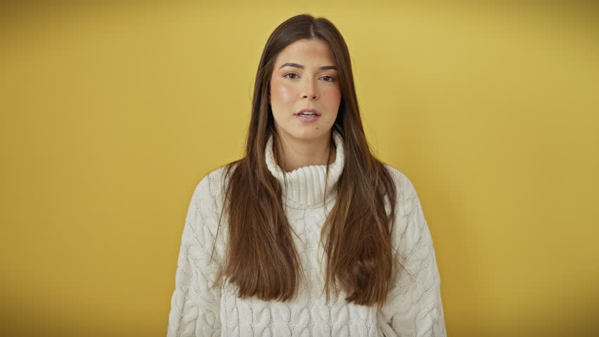 Hush! beautiful young hispanic woman wearing sweater, whispering juicy secrets. standing over isolated yellow background, hand on mouth, stirring tempting chatter conversation.
