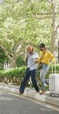 Vertical video of happy diverse couple walking with luggage in city. Vacation, on the go, out and about in the city.