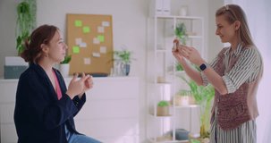 Young businesswoman filming female colleague explaining strategy on smartphone in corporate office
