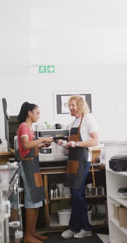 Vertical video of happy diverse male and female baristas drinking coffee in cafe. Cafe, barista and business concept.