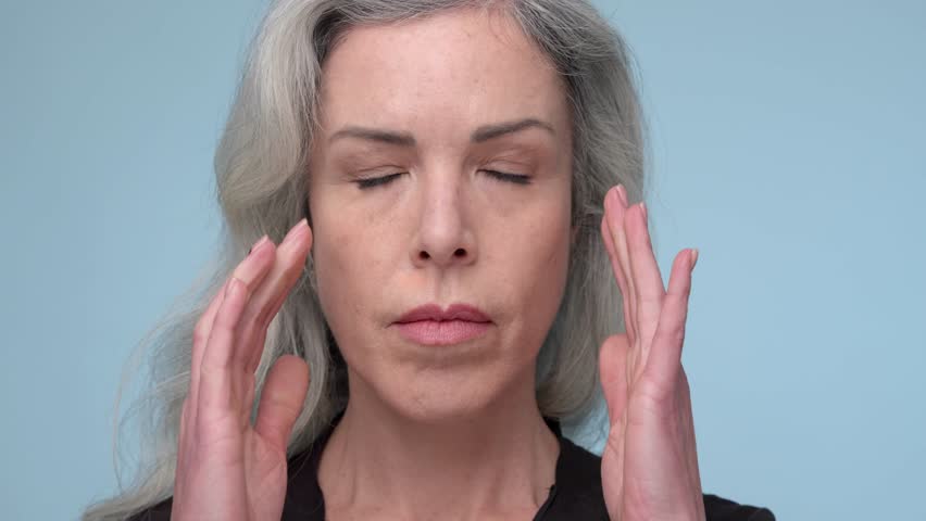 Close-up of a woman in her 40s with gray hair, resting her cheek on her fist, displaying a thoughtful or troubled expression.