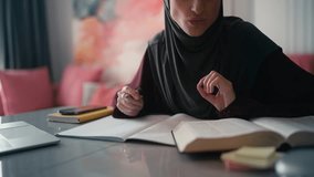 Female Arab student in hijab studying at home, reading textbook, writing notes - Powered by Shutterstock - Get 15% off with code: PIKWIZARD15