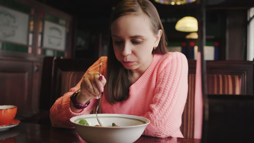 A girl sits at a table, eating from a bowl of food in a casual setting.