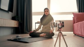 Female fitness coach in hijab streaming training online, exercising on camera