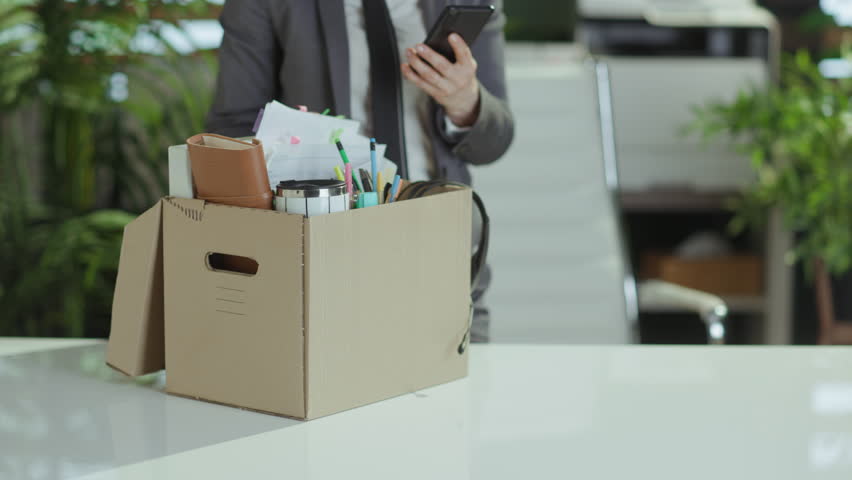 New job. stressed modern female worker in modern green office in grey business suit with personal belongings in cardboard box talking on a smartphone. Royalty-Free Stock Footage #3462651209