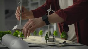 A design specialist uses a tool to professionally place a mini model of a windmill in an architectural studio. Architectural engineer designing wind turbine placement sustainable urban project - Powered by Shutterstock - Get 15% off with code: PIKWIZARD15