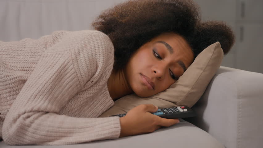 African American tired woman girl lying on couch home alone hold remote control switch channels watch TV boring weekend lonely bored lazy relax on sofa sad depressed frustrated female inactive apathy Royalty-Free Stock Footage #3462657365