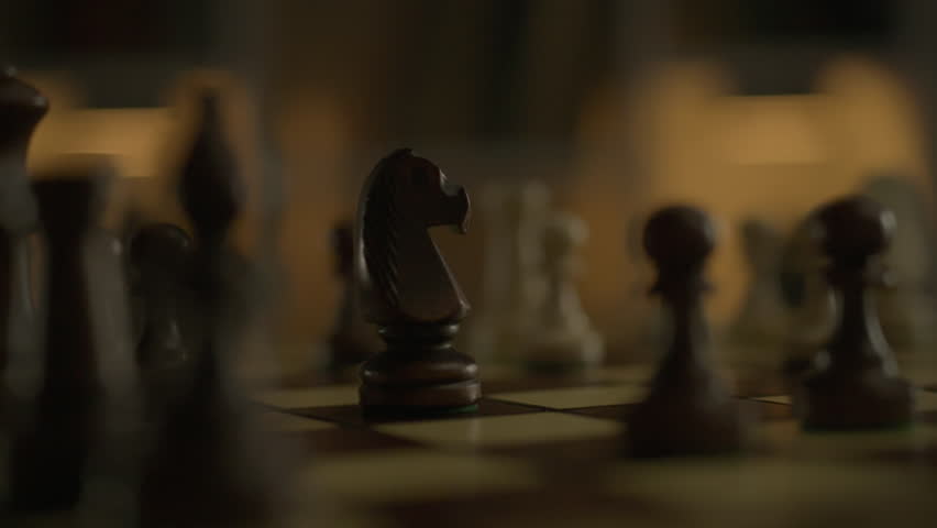 The male hand of a chess player performs a move by moving the knight chess piece across the board to the correct cell. The process of a chess battle between two professional players. Strategic battle