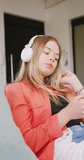 Vertical video of happy caucasian teenager girl wearing headphones, slow motion. Spending quality time at home, domestic life and friends concept.