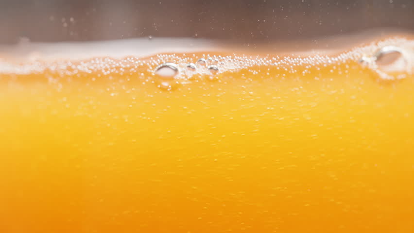 Orange Juice or Soda Macro Shot, Bubbles and Liquid Level in the Glass, Slow Motion.
