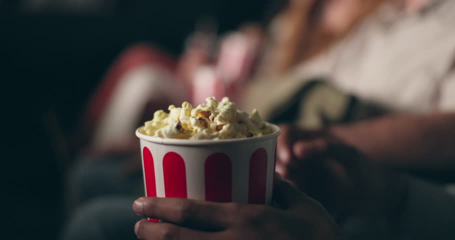 Closeup, hands and man with popcorn, cinema and movie theater with audience and snack. Eating, film treat and people with premiere and food with crowd and hungry with entertainment, relax and leisure