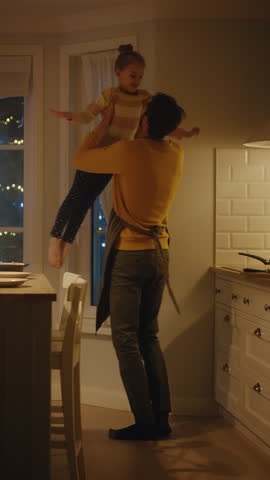 Happy Father and Daughter Cooking and Having Dinner Together. Father Prepares Food, Cute Little Girl Runs and Hugs Him, They Dance and Swirl. Video with Vertical Screen Orientation 9:16