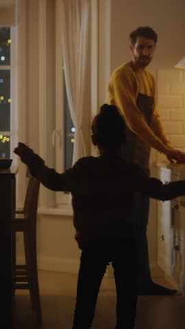 Happy Father and Daughter Cooking and Having Dinner Together. Father Prepares Food, Cute Little Girl Runs and Hugs Him, They Dance and Swirl. Video with Vertical Screen Orientation 9:16