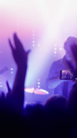 Vertical Footage of Rock Band Performing at a Concert in a Night Club. Front Row Crowd Record Video on Their Mobile Phones. Party in Front of Bright Colorful Strobing Lights on Stage.