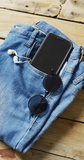 Vertical video of denim trousers with sunglasses, smartphone and earphones with copy space. Denim, clothes and fashion concept.