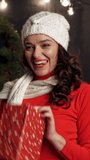 Happy girl on bed tossing a gift box. Beautiful young woman in knitted cap holding Christmas presents and having fun at home. New Year time. Vertical video