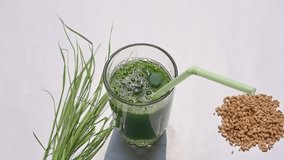 Wheatgrass juice on white background. Healthy organic green detox juice from grass of green germinated wheat grains. Healthy drink. Green leaves of young wheat and wheat grass juice. Slow motion video