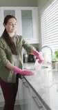 Vertical video of happy caucasian woman wearing rubber gloves and cleaning in kitchen. Spending quality time at home concept.
