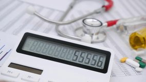 Calculator with changing numbers on display and red stethoscope with medical drugs on financial data. Cost of medicine and health insurance concept. - Powered by Shutterstock - Get 15% off with code: PIKWIZARD15