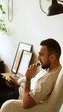 handsome bearded guy sitting in sheep wool chair in room smoking vape and talking. vertical video