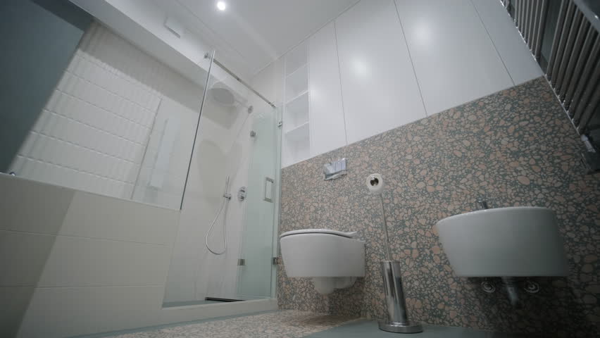 A contemporary bathroom features a spacious walk-in shower with white tiling, a unique terrazzo accent wall, and minimalist fixtures, creating an elegant and serene atmosphere Royalty-Free Stock Footage #3463139487