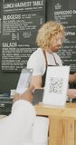 Vertical video of happy diverse male barista and woman scanning qr code with smartphone in cafe. Cafe, barista and business concept.