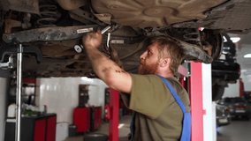 Auto mechanic repairs car suspension in garage. Skilled technician uses wrench under vehicle, focuses on fixing shock absorbers. Auto service shop scene with repairman working on lift. - Powered by Shutterstock - Get 15% off with code: PIKWIZARD15