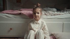 Cute girl sitting on on floor in bedroom and looking at camera.
