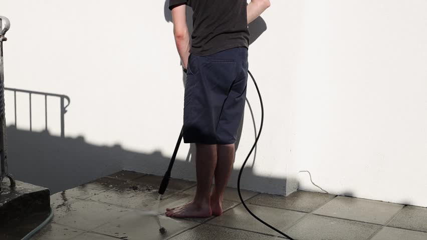 A young man washes garden tiles in his yard using a Karcher.
