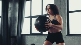 Young athletic curly woman in sportswear passes medicine ball in motion to partner or core strength training in gym. Concept of professional sportsman, healthy lifestyle, workout. Ad