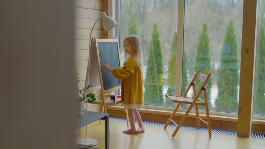 A child in a linen dress drawing butterflies on a chalk board in a wooden house.