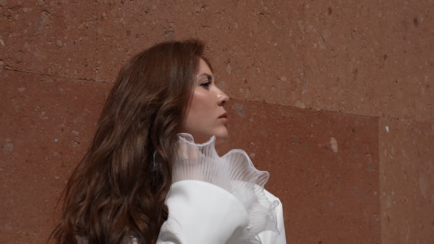 A happy woman in formal wear gestures in front of a white wall at a fun event
