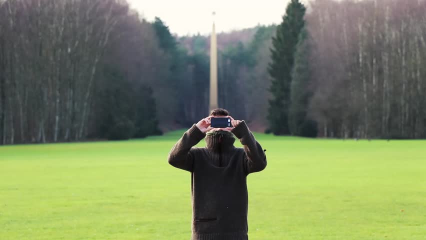 young man taking picture with smart phone in the park 