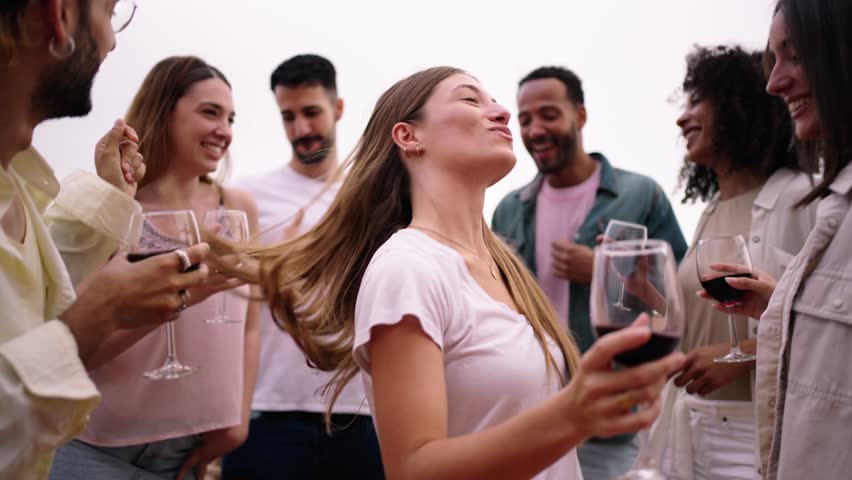 Pretty blonde woman looking flirtatious at camera and dancing with group excited multiracial friends meeting celebrating together with glasses of red wine at penthouse party. People enjoying vacation Royalty-Free Stock Footage #3463396345