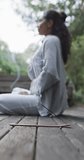 Vertical video of focused biracial woman practicing yoga in sunny garden, slow motion. Lifestyle, wellbeing in nature, yoga, fitness, healthy lifestyle and domestic life, unaltered.