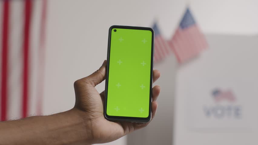 Close-up of hand-holding green screen mobile phone in front of the ballot box in the American election. Royalty-Free Stock Footage #3463507449