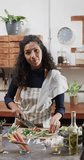 Vertical video of portrait of happy biracial woman chopping vegetables in kitchen, slow motion. Lifestyle, food, cooking, healthy lifestyle and domestic lifestyle, unaltered.