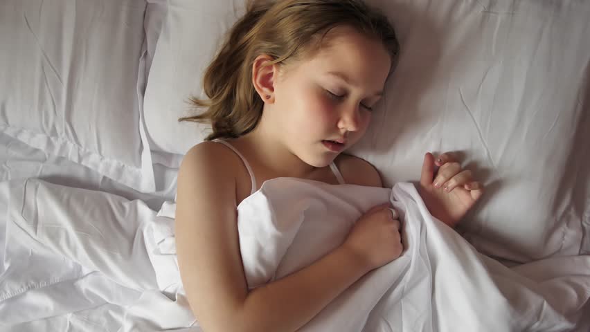 Top view of a girl with brown hair sleeping on a bed with white linen and white pillows. Cute sleeping baby. Healthy good children