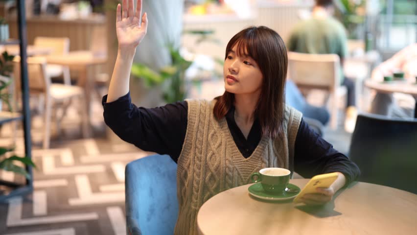 Greeting friends with a bright smile. Cheerful Woman Waving in Sunlit Cafe