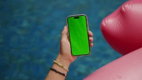 POV male hand holding smartphone with empty green screen chroma key relaxing near pool with pink flamingo background  - Powered by Shutterstock - Get 15% off with code: PIKWIZARD15