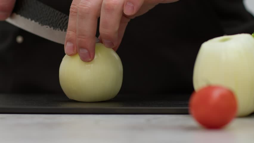 Close-up of white onion. The cook cuts the onion into rings; the onion lies in neat half rings on the board. Slow-motion video of a chef confidently chopping vegetables with a kitchen knife.